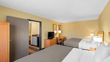 A hotel room with two beds, a desk with a television, a chair, and a small table with a lamp.