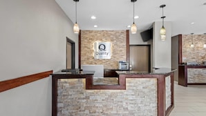 A reception desk with a stone facade, a 'Quality by Choice Hotels' sign, and pendant lighting. - Quality Inn & Suites Des Moines Airport (Des Moines)