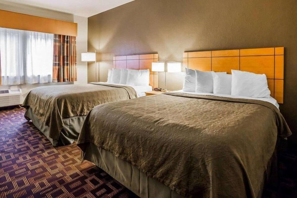A hotel room with two beds, a large window with curtains, and a patterned carpet.