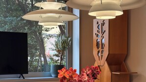 A modern room with a large window, a flat-screen TV, a vase with flowers, a lamp, and a chair. - Garden Hotel Michelangelo (Mestre)