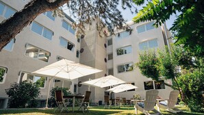 An outdoor patio area with multiple chairs and tables under umbrellas, surrounded by greenery and a building with multiple windows. - Garden Hotel Michelangelo (Mestre)