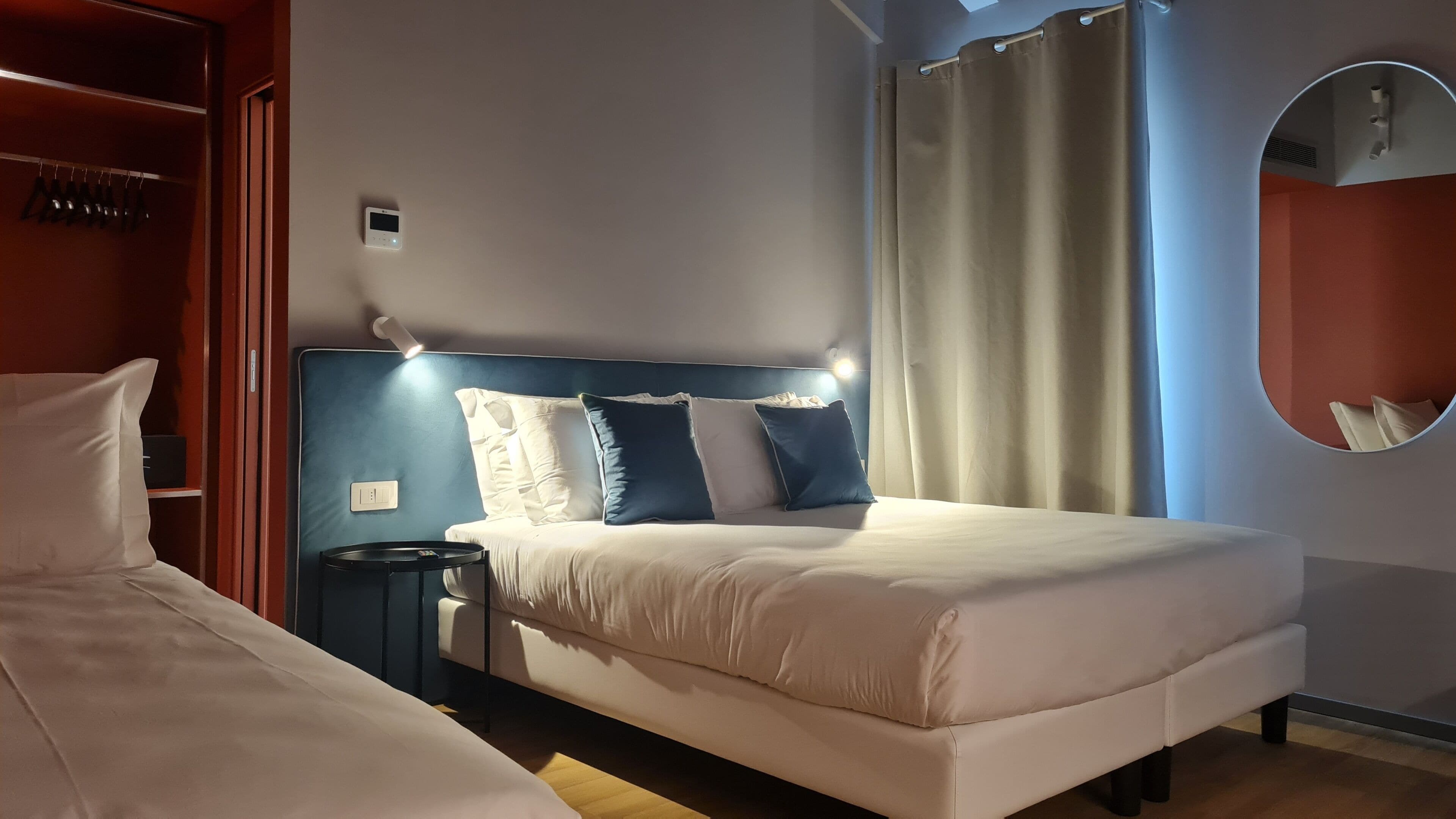 A bedroom with a bed, bedside table, and a wall-mounted thermostat.