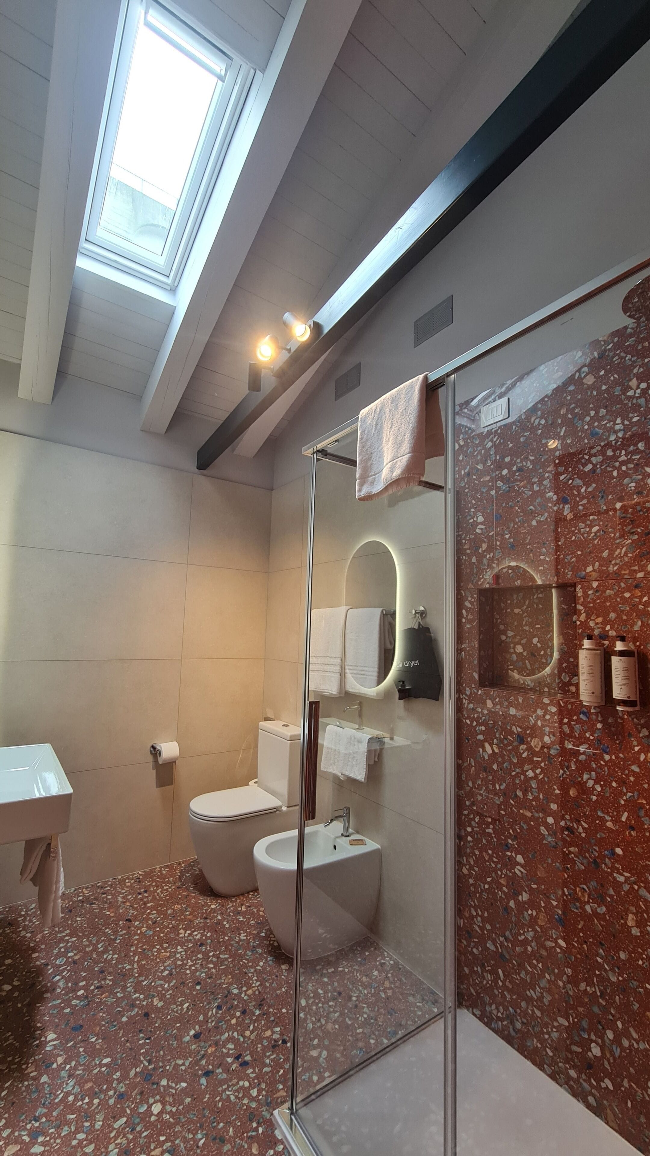 A modern bathroom with a skylight, a glass-enclosed shower, a toilet, and a sink.