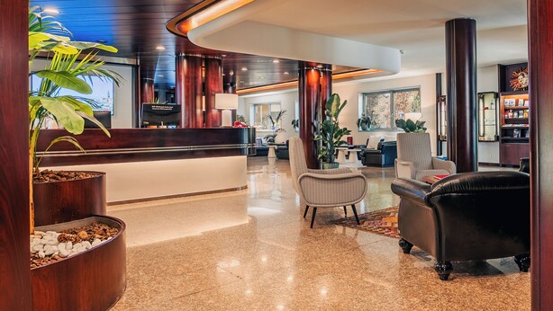 A modern hotel lobby with a reception desk, seating area, and decorative plants. - Garden Hotel Michelangelo (Mestre)