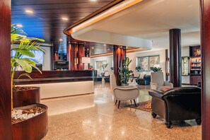 A modern hotel lobby with a reception desk, seating area, and decorative plants. - Garden Hotel Michelangelo (Mestre)