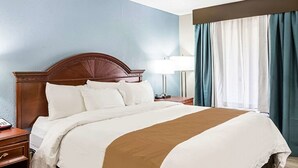 A hotel room with a large bed, a wooden headboard, a nightstand, a lamp, and a window with curtains. - Farragut Inn & Suites (Farragut)