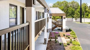 A building with a covered outdoor area, a staircase leading to an upper level, and a landscaped garden with various plants and flowers. - Farragut Inn & Suites (Farragut)