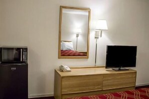 A hotel room with a microwave, a TV on a wooden dresser, a mirror, and a lamp. - Econo Lodge (Columbus)