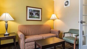 Une chambre d’hôtel avec un canapé à motifs, une petite table, deux lampes, une chaise et un tableau encadré au mur.