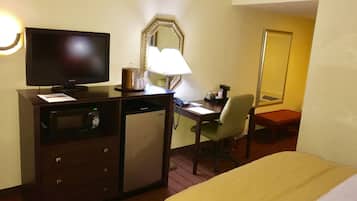 Une chambre d’hôtel équipée d’un lit, d’un bureau avec un ordinateur, d’une télévision, d’un four à micro-ondes, d’une lampe et d’un miroir.