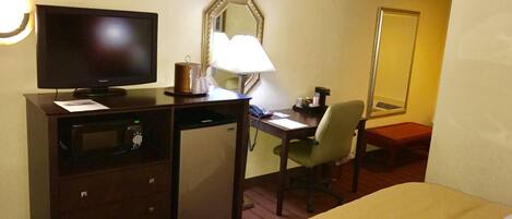 Habitación de hotel con cama, escritorio con computadora, televisión, microondas, lámpara y espejo.