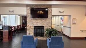 Un hall d’entrée avec une cheminée en pierre, un téléviseur à écran plat et deux fauteuils bleus.