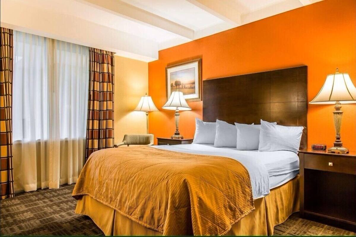 Una habitación de hotel con una cama grande, dos lámparas de noche, una mesita de noche y una ventana con cortinas.