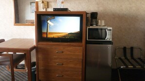 Ein kleiner Raum mit Fernseher auf einem Holzschrank, einer Mikrowelle, einer Kaffeemaschine und einem Sessel.