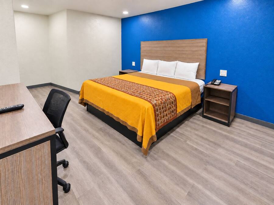 Een hotelkamer met een bed, nachtkastje, stoel en een bureau met een afstandsbediening.