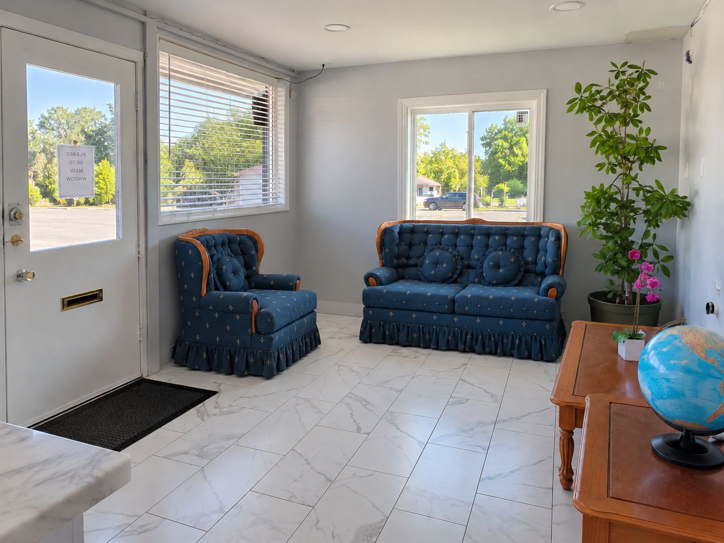 Ein Zimmer mit einem blauen Sofa, einem Holztisch mit Globus, einer Topfpflanze und einer Tür mit Fenster.