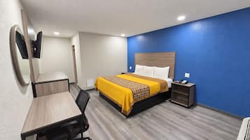 A hotel room with a bed, desk, chair, bedside table, and a mirror.