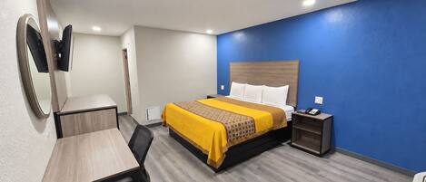 A hotel room with a bed, desk, chair, bedside table, and a mirror.