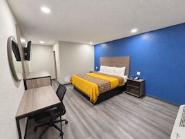 Quarto de hotel com cama, escrivaninha, cadeira, mesa de cabeceira e espelho.