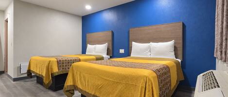 A hotel room with two beds, each with a headboard, a bedside table, and a heater.