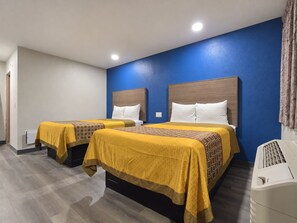 A hotel room with two beds, each with a headboard, a bedside table, and a heater.