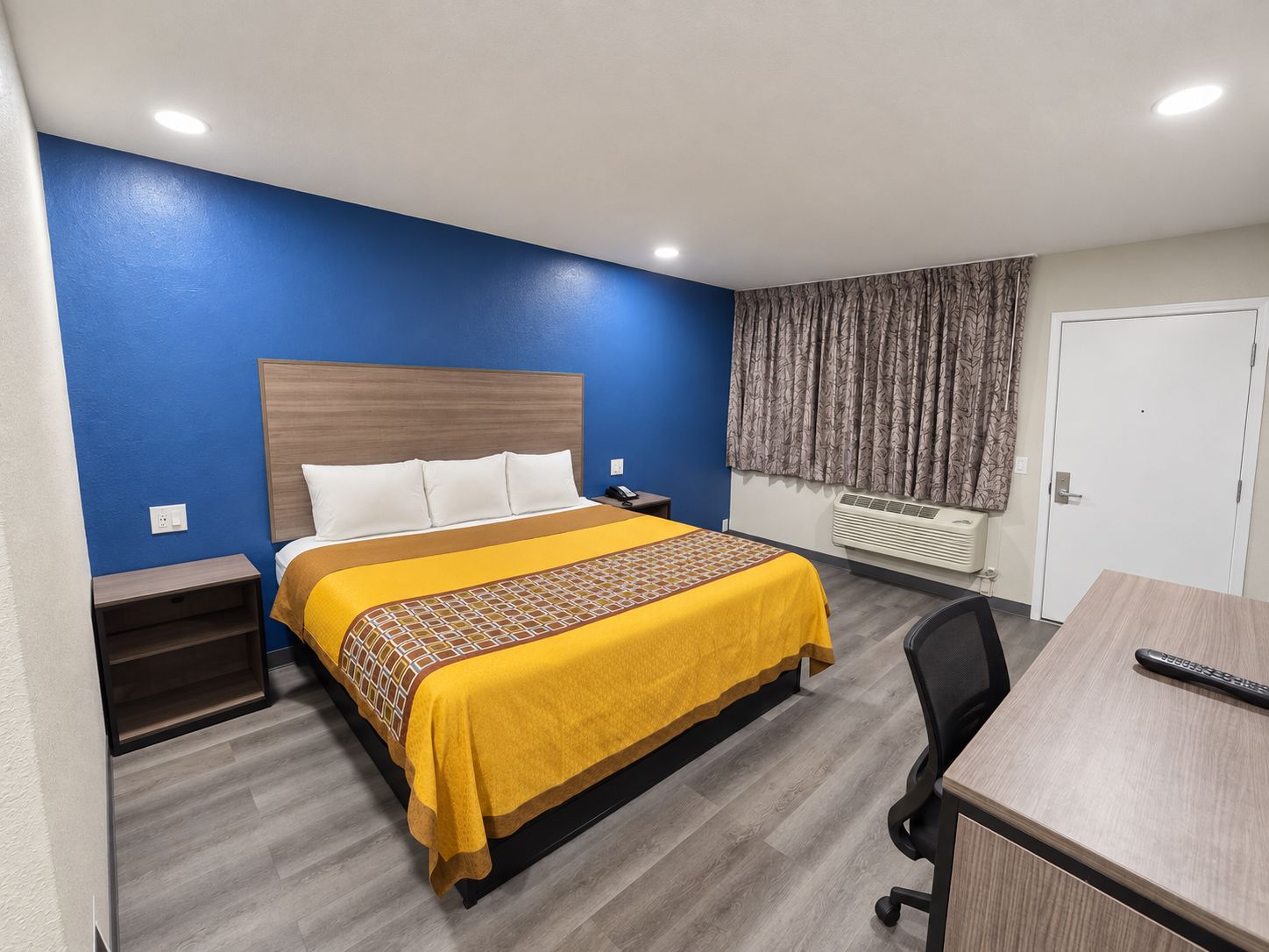 A hotel room with a bed, bedside table, desk, chair, and a door.