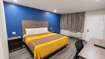 A hotel room with a bed, bedside table, desk, chair, and a door.