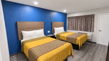 A hotel room with two beds, each with a wooden headboard, white pillows, and yellow bedspreads with a geometric pattern.