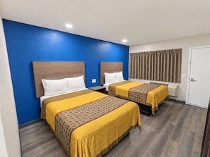 A hotel room with two beds, a blue accent wall, and a window with curtains.