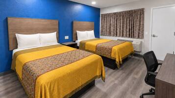 A hotel room with two beds, a desk, a chair, a wardrobe, and a window with curtains.