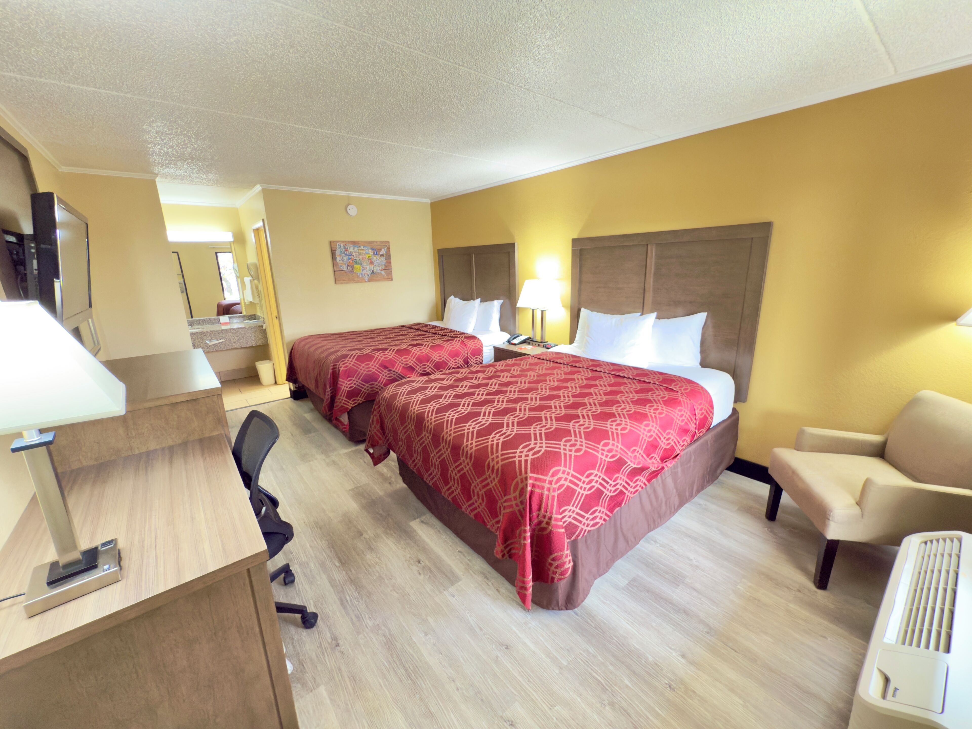 A hotel room with two beds, a desk, a chair, a lamp, and a map on the wall.