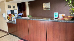 A hotel reception desk with a digital screen, framed certificates, a welcome sign, and a sign indicating complimentary breakfast times. - Econo Lodge Lenoir City - Knoxville Area (Lenoir City)