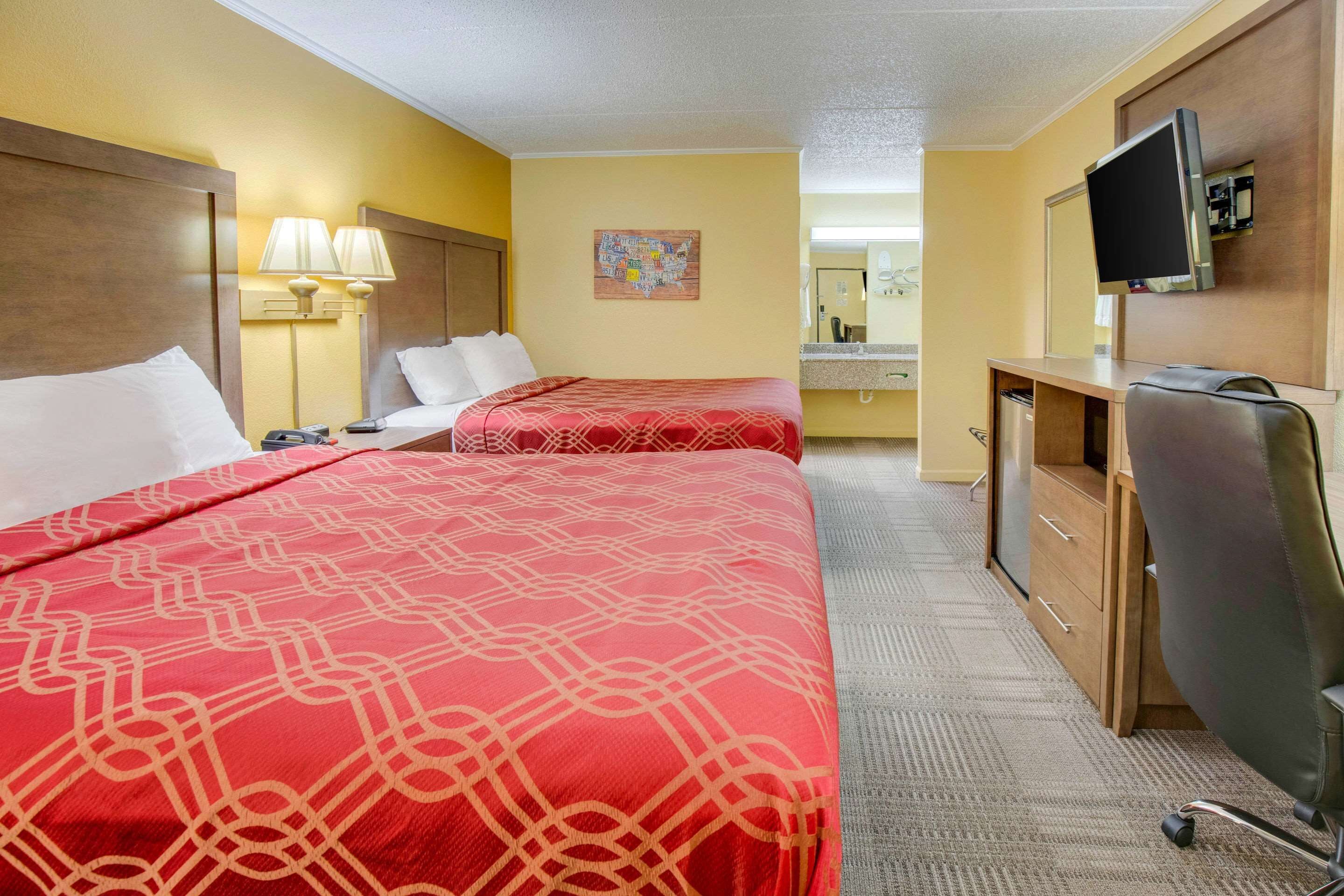 A hotel room with two beds, a desk, a television, and a bathroom visible in the background.