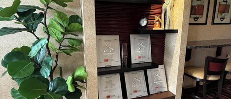 A reception area with a potted plant, a shelf displaying awards, and a clock.