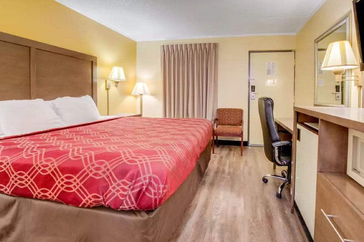 A hotel room with a large bed, a desk, a chair, and a mirror.