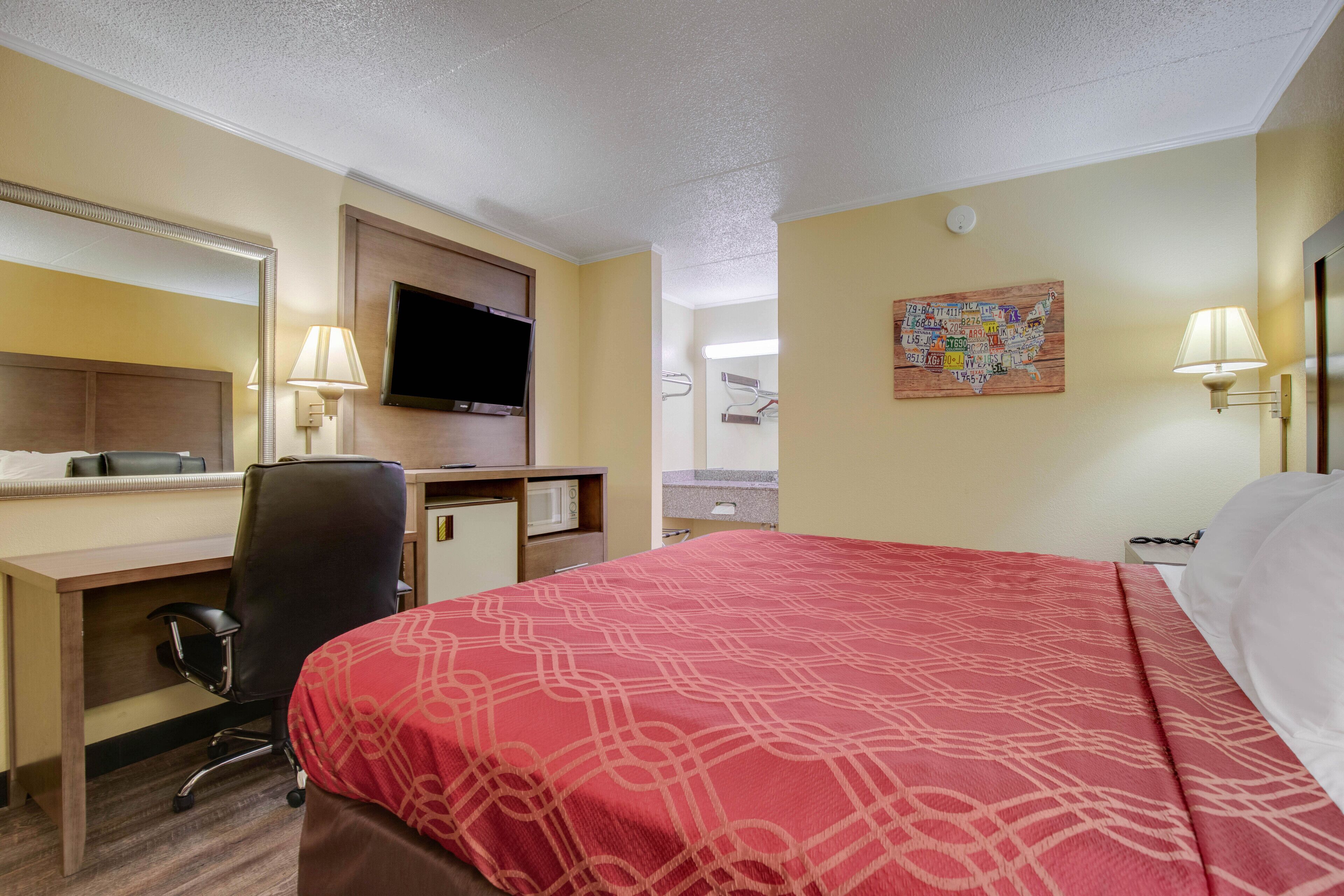 Habitación de hotel con cama, escritorio, silla, televisor y una obra de arte en la pared.