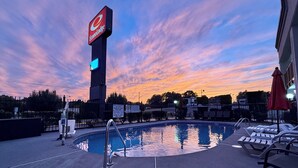 A swimming pool with lounge chairs, a sign for EconoLodge, and a sunset sky. - Econo Lodge Lenoir City - Knoxville Area (Lenoir City)
