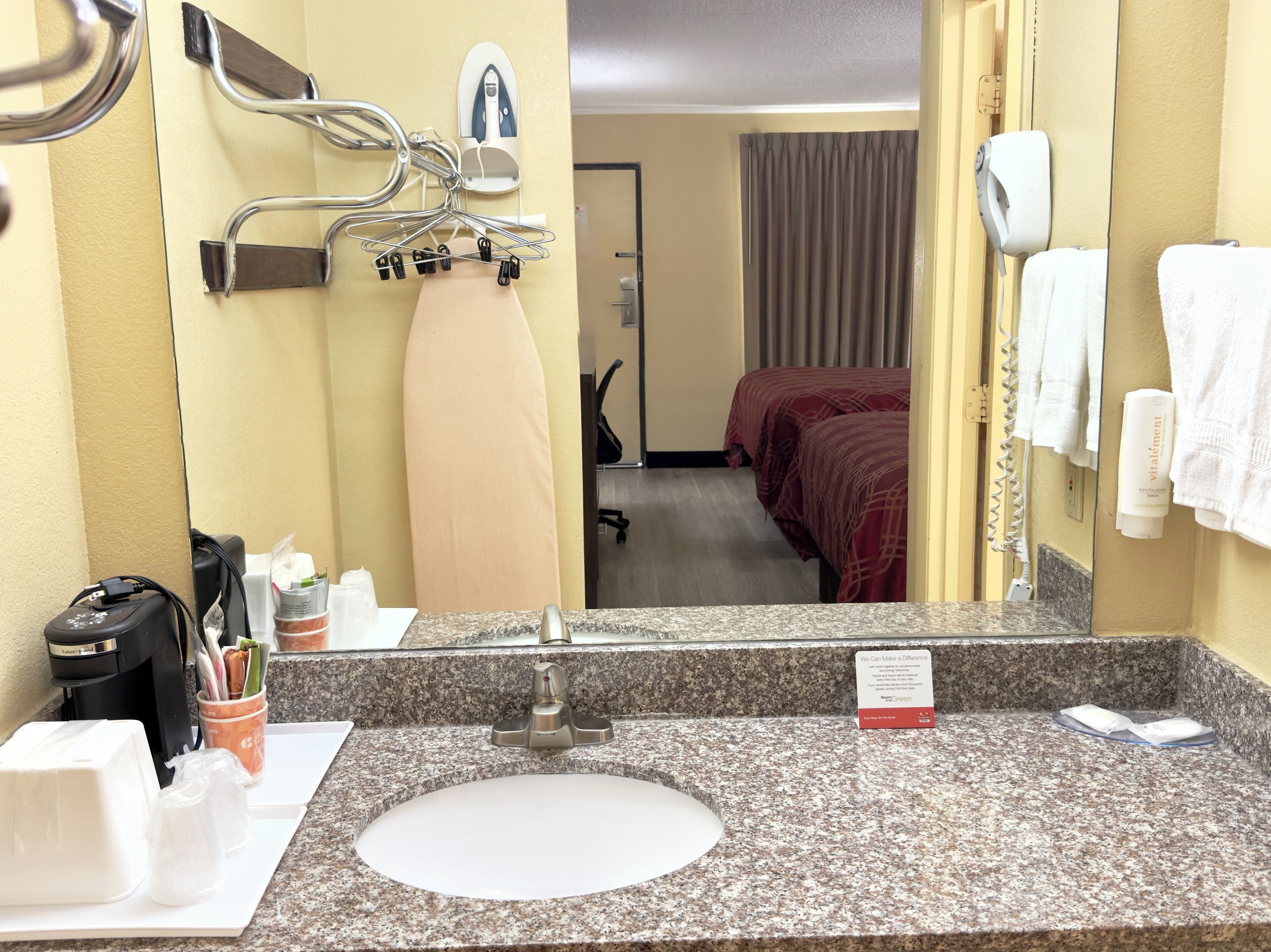 Et badeværelse på et hotel med en vask med granitbordplade, et spejl, en hårtørrer og en håndklædestang.