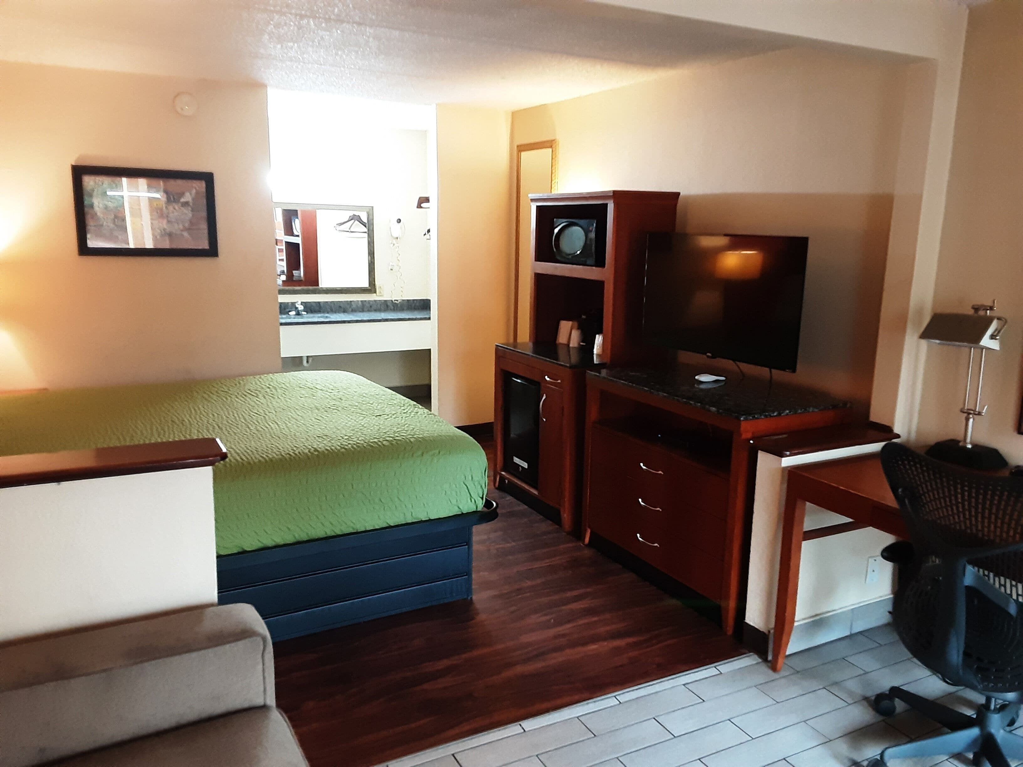 Habitación de hotel compacta con cama, escritorio con ordenador, televisor y una silla.