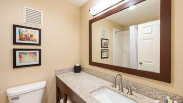 A bathroom with a sink, mirror, toilet, and framed pictures on the wall.