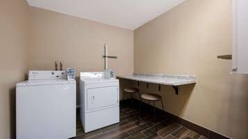 A laundry area with two Whirlpool washers and dryers, a small bar stool, and a countertop.