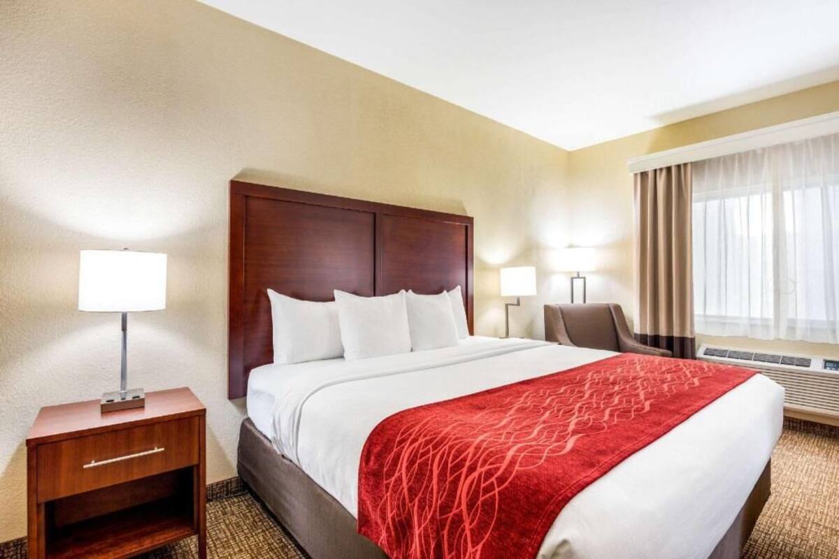 A hotel room with a large bed, two bedside tables with lamps, a chair, and a window with curtains.