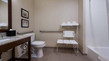 A bathroom with a toilet, sink, and shower. There are two framed pictures on the wall, a towel rack with towels, and a white chair.