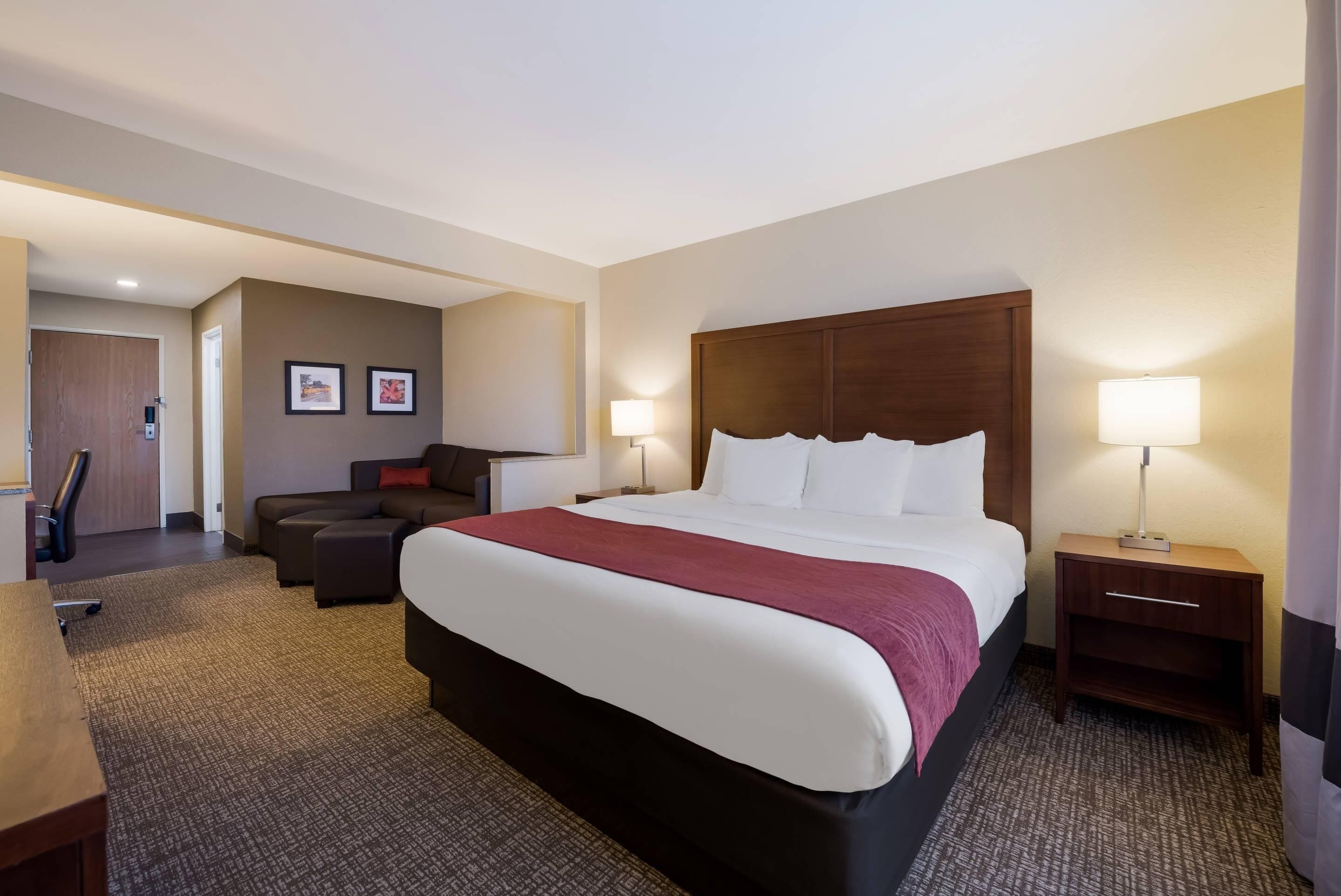 A hotel room with a large bed, a desk, a chair, a sofa, and two bedside lamps.
