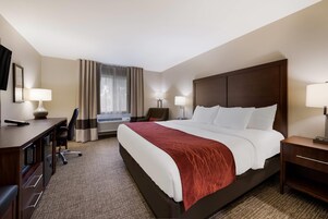 Habitación de hotel con una cama grande, un escritorio con lámpara, una silla, una lámpara de escritorio y una ventana con cortinas.