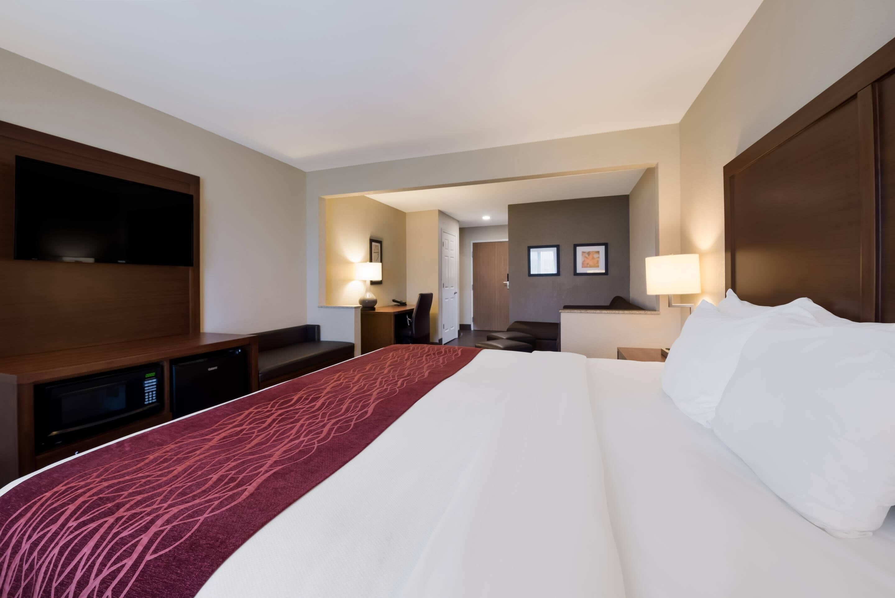 Une chambre d’hôtel dotée d’un grand lit, d’un téléviseur à écran plat fixé au mur, d’un bureau avec une lampe et d’un petit coin cuisine.