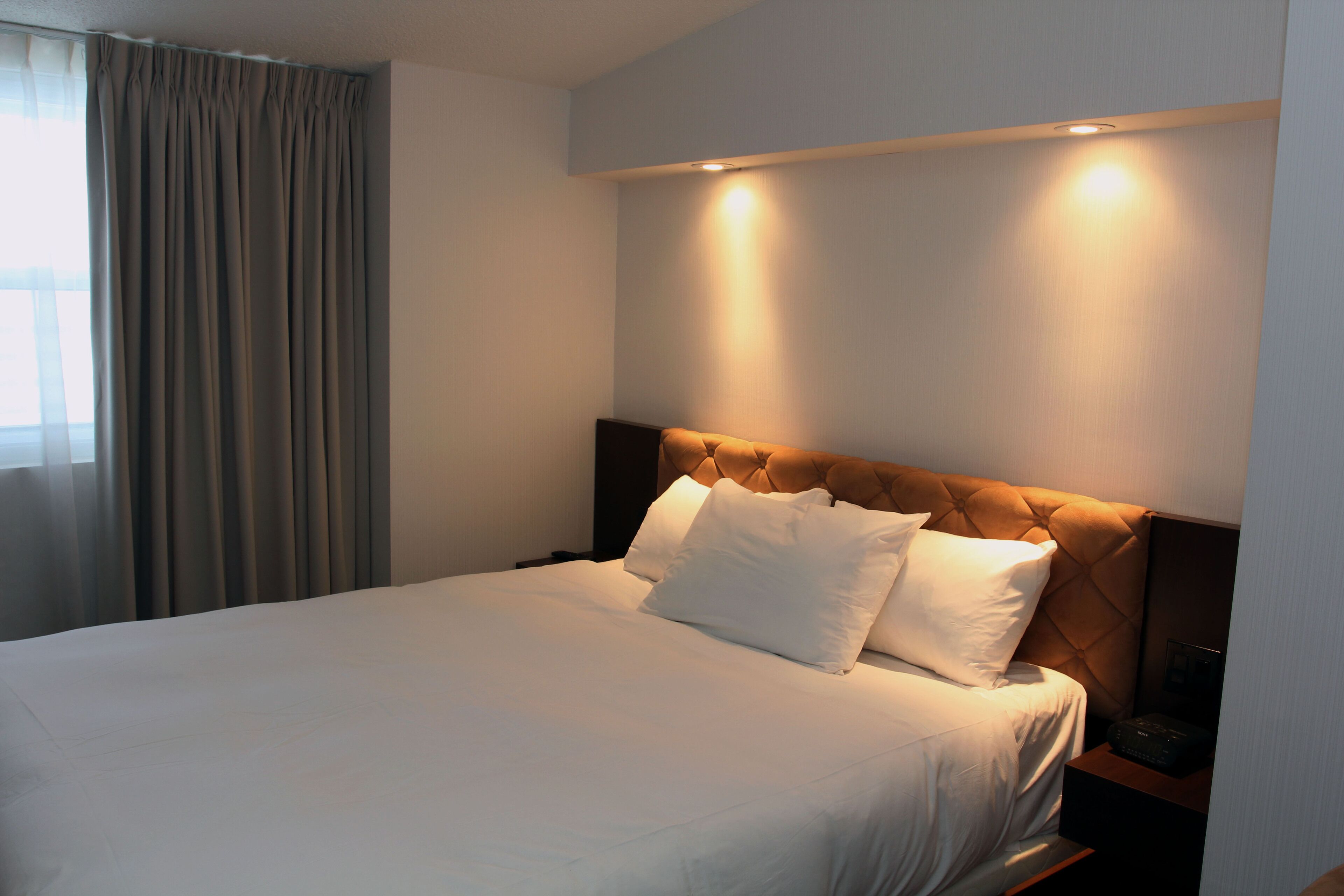 A neatly made bed with a headboard, a bedside table, and a lamp.
