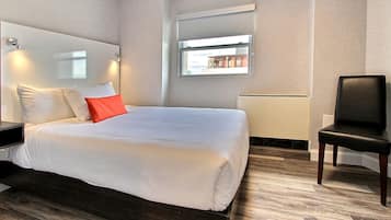 A modern hotel room with a large bed, a chair, a window with a view, and a mirror on the wall.