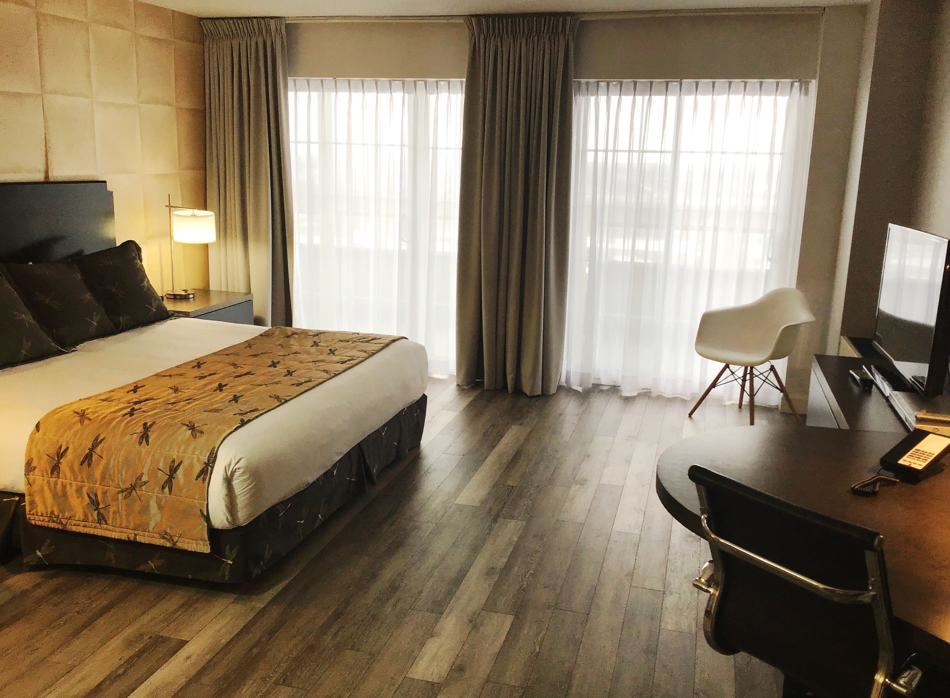 Une chambre d’hôtel avec un grand lit, un bureau avec une chaise, une télévision et une fenêtre avec des rideaux.