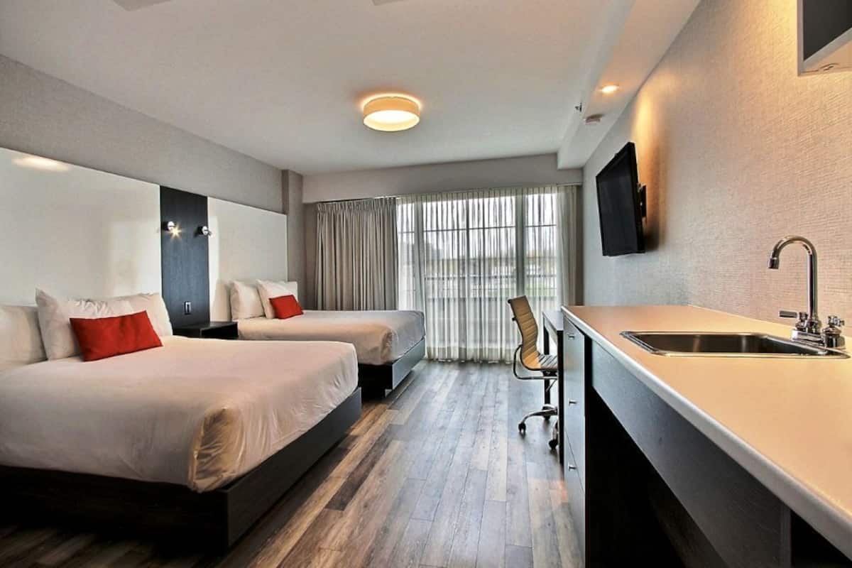 A hotel room with two beds, a desk with a sink, a chair, and a TV mounted on the wall.